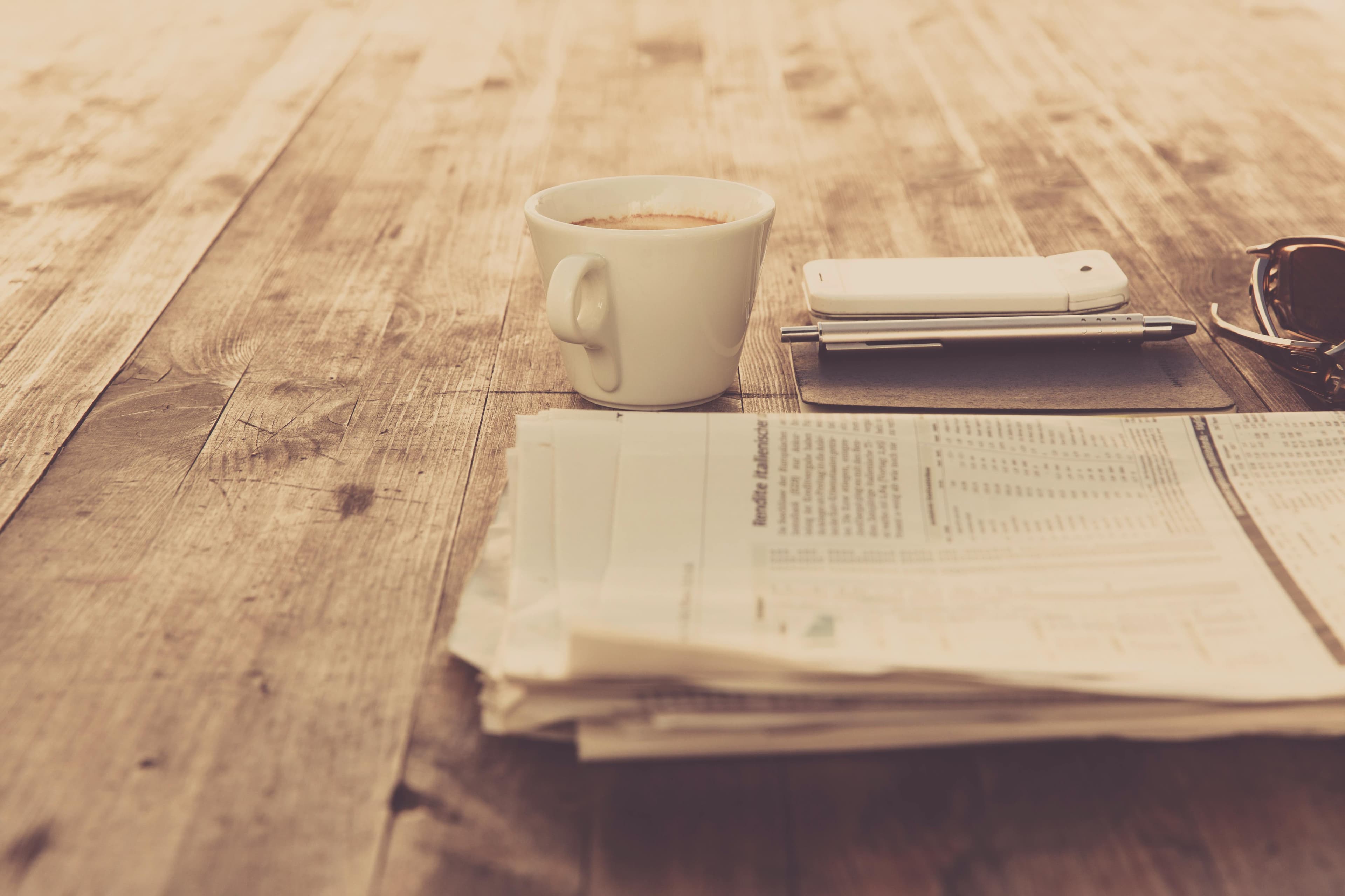Coffee cup and newspaper on wooden table